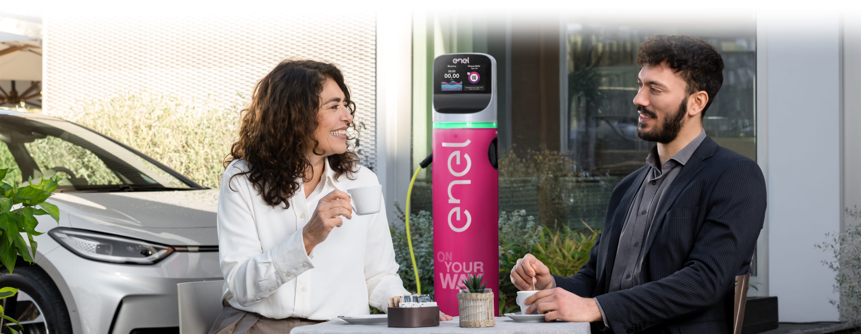 auto in ricarica con colonnina enel x nello sfondo una ragazza al cellulare