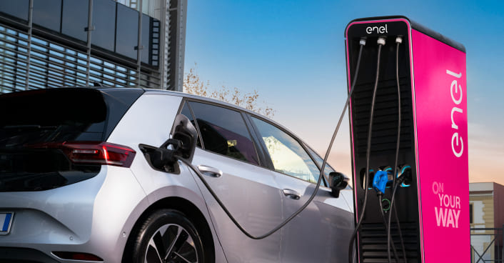 auto in ricarica con colonnina enel x nello sfondo una ragazza al cellulare