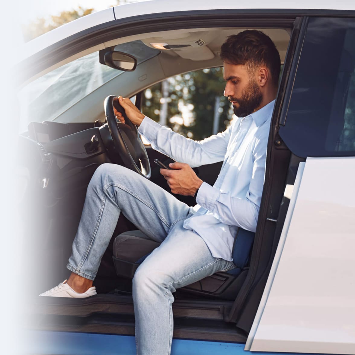 immagine ragazzo al cellulare seduto al posto di guida su una macchina bianca