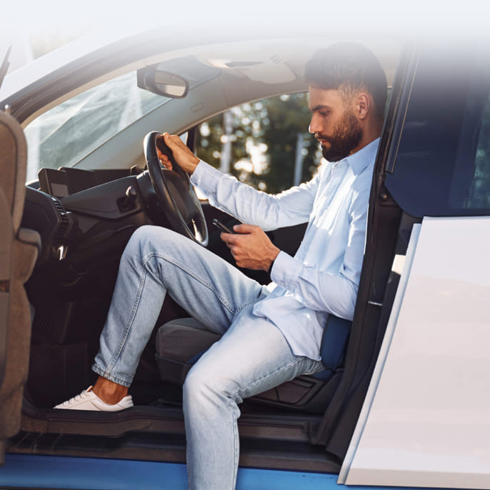immagine ragazzo al cellulare seduto al posto di guida su una macchina bianca