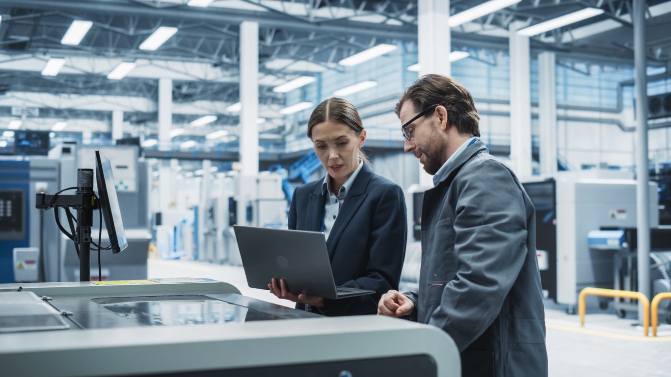 Manager femminile con un laptop e parla con l'ingegnere industriale maschio presso una moderna fabbrica di elettronica.