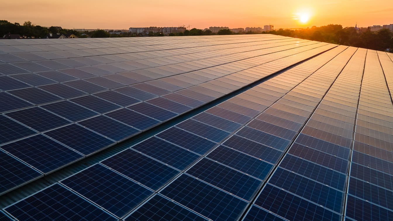 vasto impianto di pannelli solari fotovoltaici installato sul tetto di una struttura industriale durante il tramonto